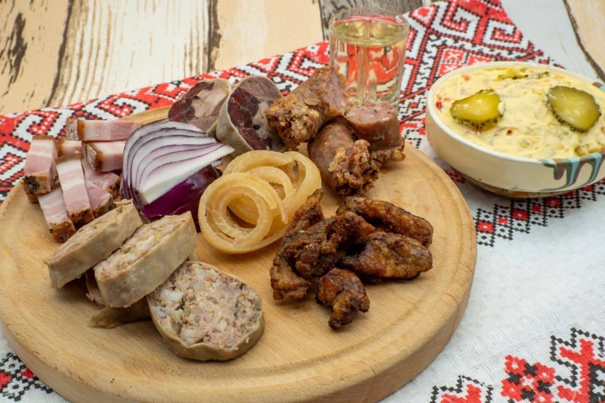 Platou cu bucate traditionale alaturi de un pahar de horinca pe stergar rustic