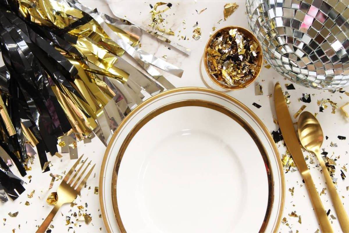 masa festiva de Revelion cu tacamuri aurii, vesele alba cu auriu si confetti